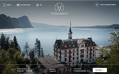 Historisches Hotel am Ufer eines Sees mit Bergen im Hintergrund.